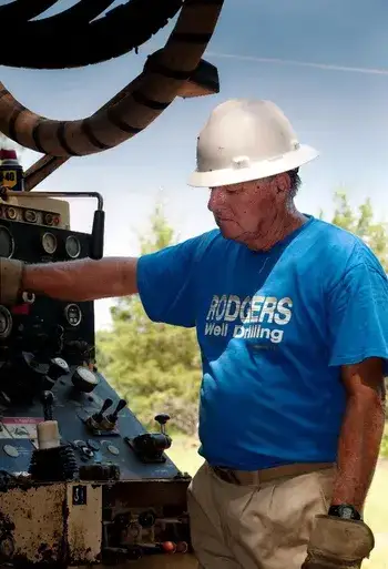Driller in a blue t-shirt and white hard hat operating a driller.